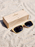 Load image into Gallery viewer, Maple wooden sunglasses with black polarized lenses and a box on sandy beach.