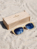 Load image into Gallery viewer, Maple wooden sunglasses with silver polarized lenses and a box on sandy beach.