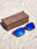 Load image into Gallery viewer, Wenge wooden sunglasses with blue polarized lenses and a box on sandy beach.