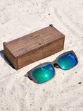 Load image into Gallery viewer, Wenge wooden sunglasses with green polarized lenses and a box on sandy beach.