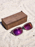 Load image into Gallery viewer, Wenge wooden sunglasses with red polarized lenses and a box on sandy beach.