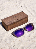 Load image into Gallery viewer, Wenge wooden sunglasses with purple polarized lenses and a box on sandy beach.