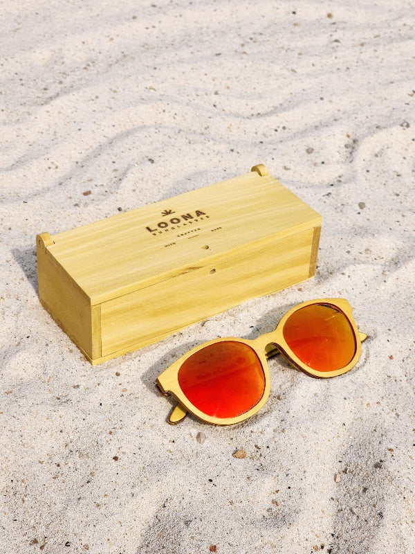 Yellowheart wooden sunglasses with red polarized lenses and a box on sandy beach.