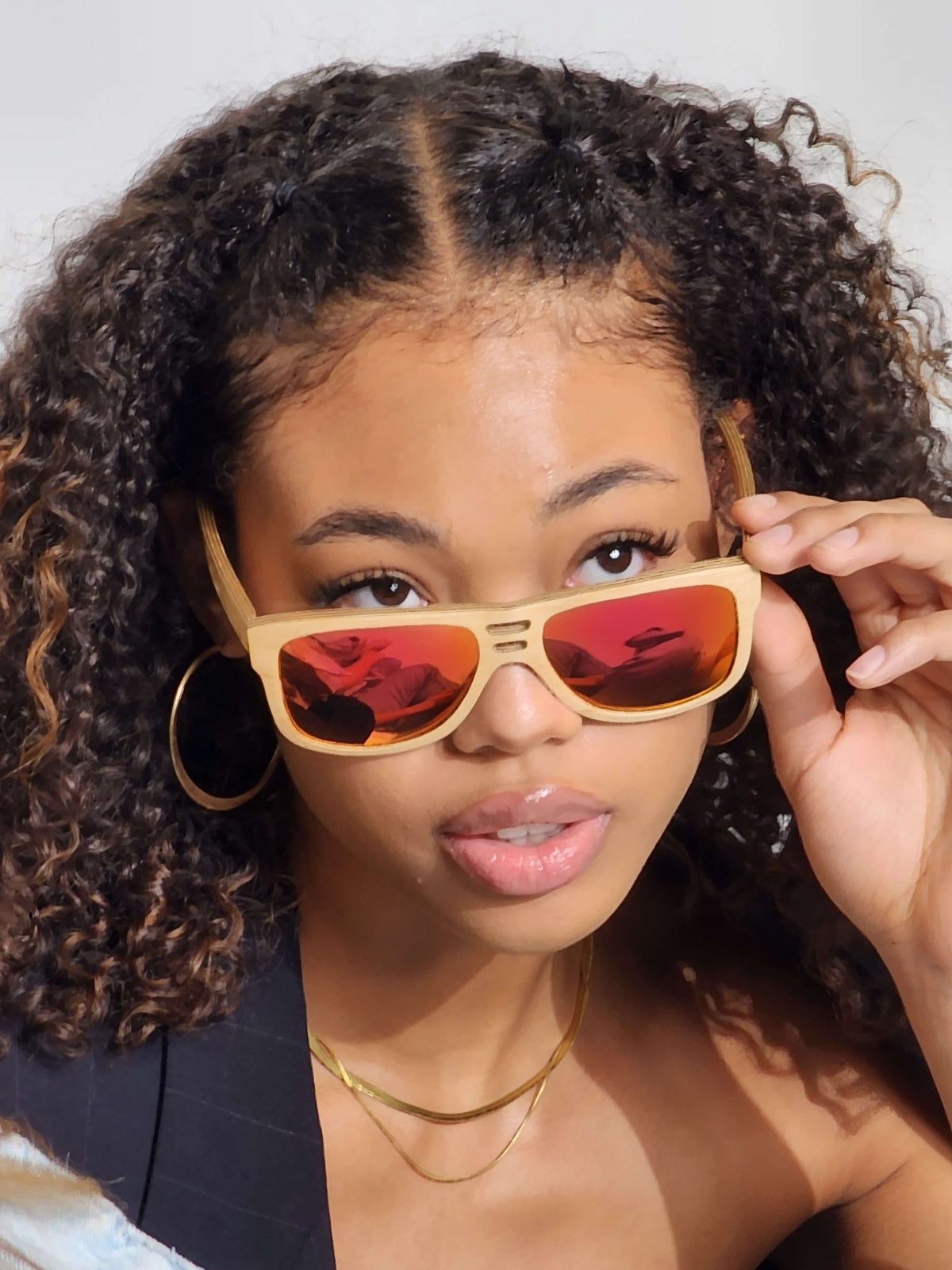 A woman with curly hair wearing wooden sunglasses, exuding style and confidence.