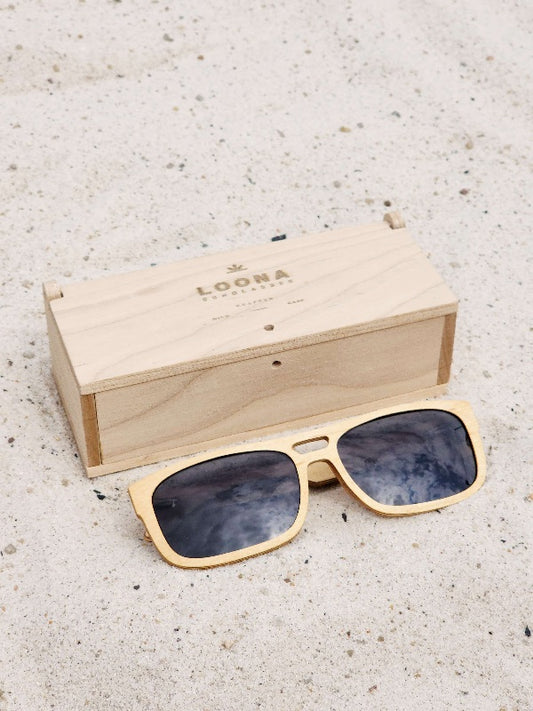 Maple wooden sunglasses with black polarized lenses and a box on sandy beach.