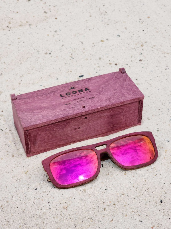 Purpleheart wooden sunglasses with red polarized lenses and a box on sandy beach.
