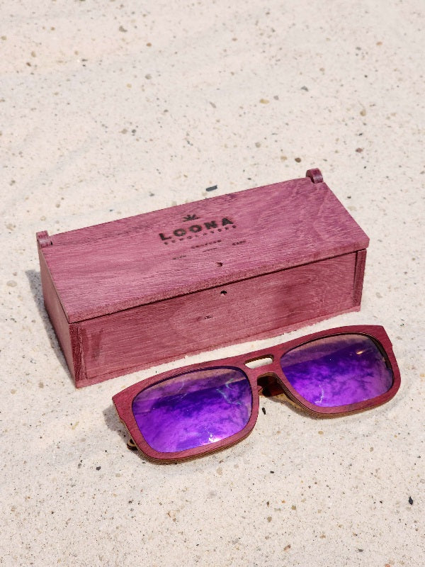 Purpleheart wooden sunglasses with purple polarized lenses and a box on sandy beach.