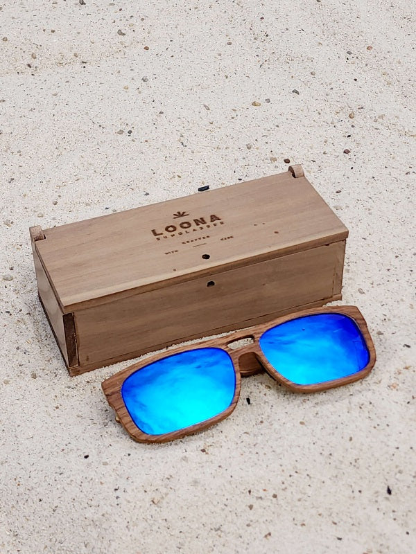 Walnut wooden sunglasses with blue polarized lenses and a box on sandy beach.