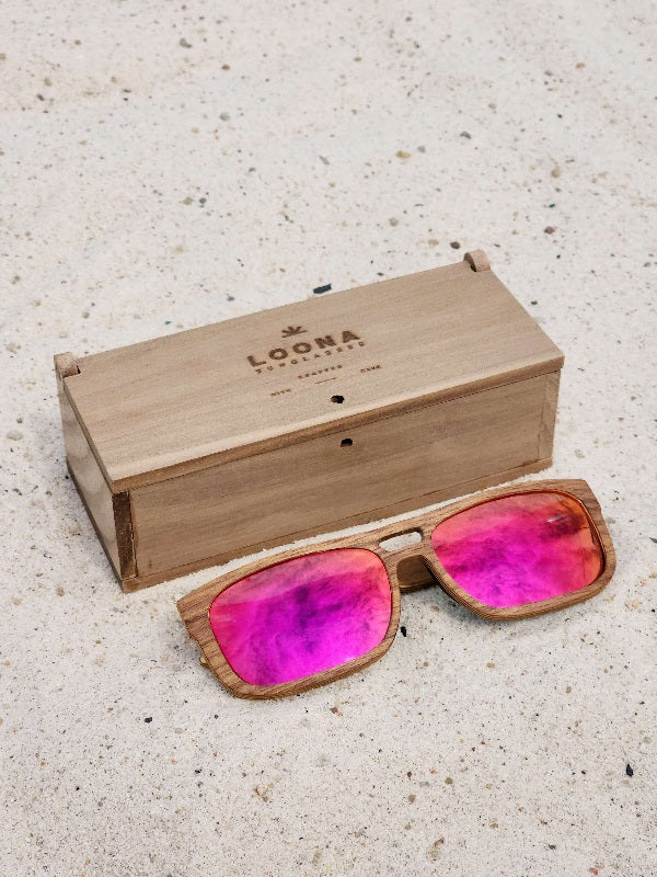 Walnut wooden sunglasses with red polarized lenses and a box on sandy beach.