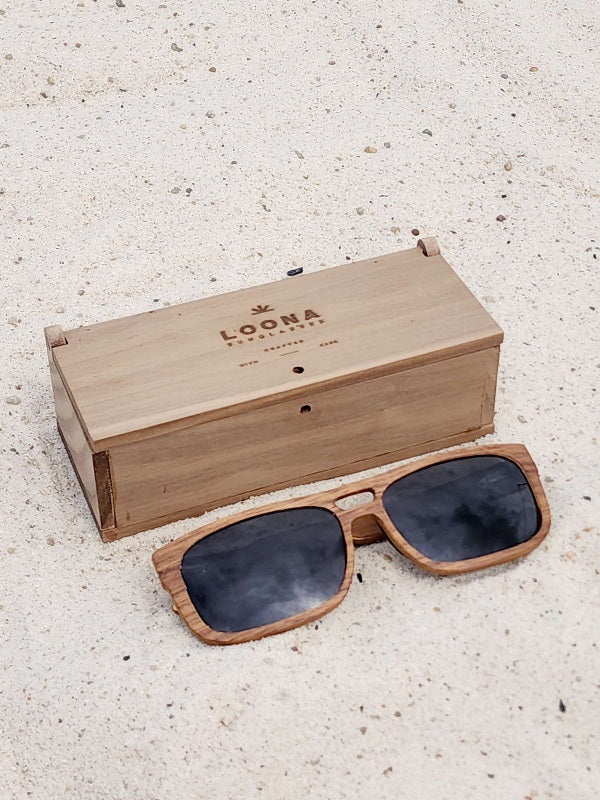 Walnut wooden sunglasses with black polarized lenses and a box on sandy beach.