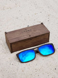 Load image into Gallery viewer, Wenge wooden sunglasses with blue polarized lenses and a box on sandy beach.

