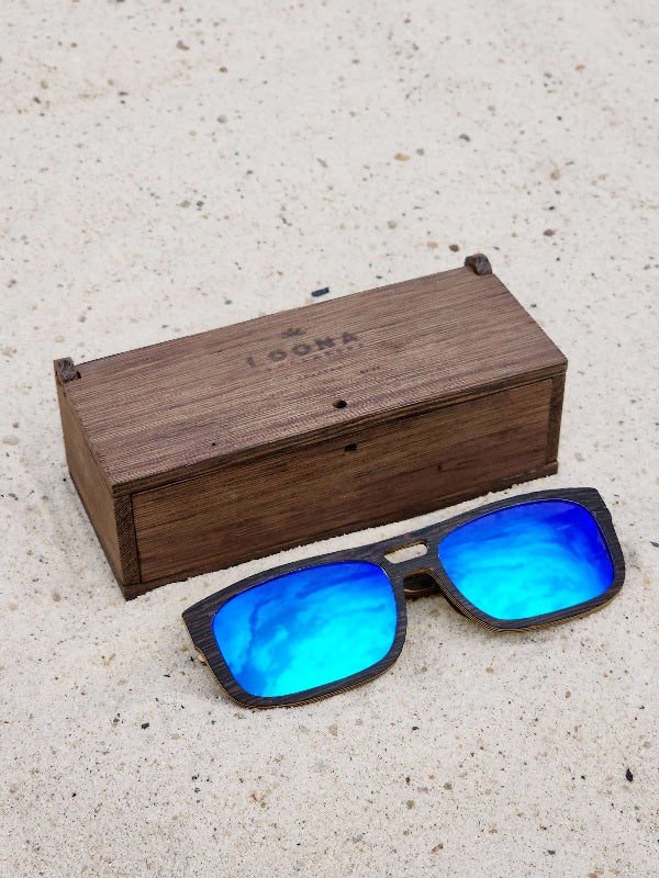 Wenge wooden sunglasses with blue polarized lenses and a box on sandy beach.