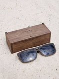 Load image into Gallery viewer, Wenge wooden sunglasses with black polarized lenses and a box on sandy beach.
