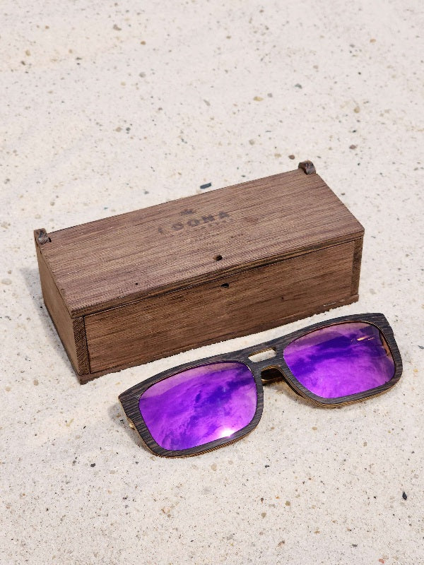 Wenge wooden sunglasses with purple polarized lenses and a box on sandy beach.