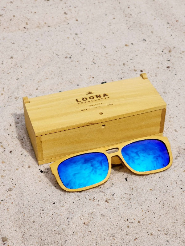 Yellowheart wooden sunglasses with blue polarized lenses and a box on sandy beach.
