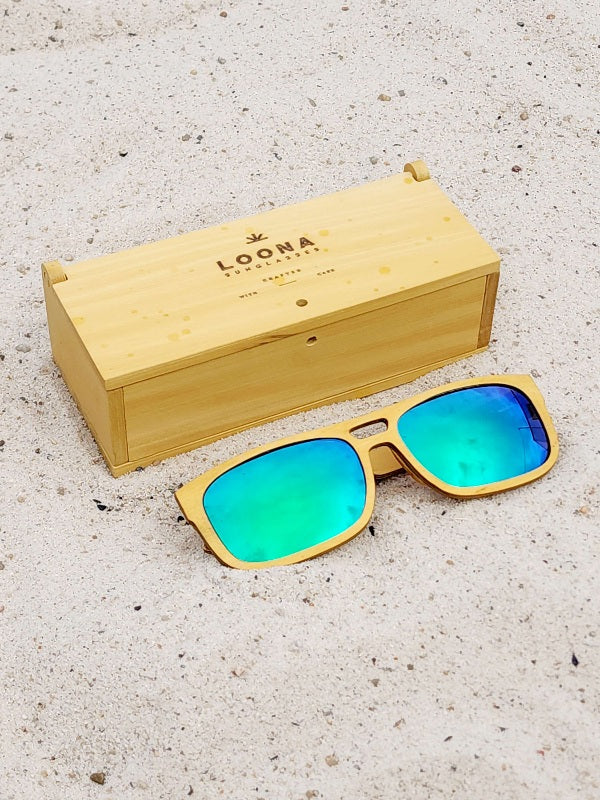 Yellowheart wooden sunglasses with green polarized lenses and a box on sandy beach.
