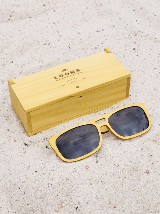 Yellowheart wooden sunglasses with black polarized lenses and a box on sandy beach.
