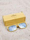 Load image into Gallery viewer, Yellowheart wooden sunglasses with silver polarized lenses and a box on sandy beach.
