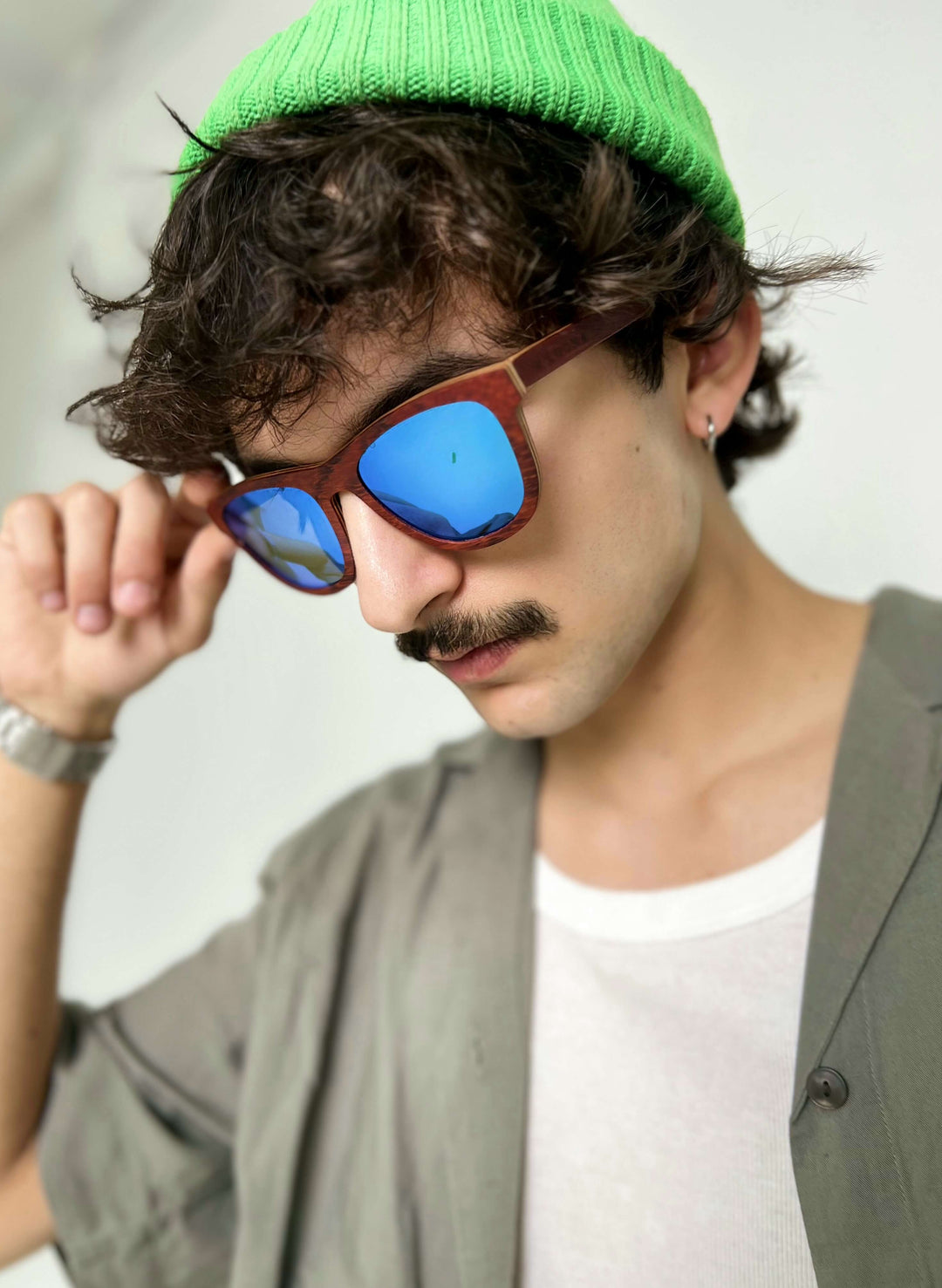 A man with a mustache wearing Handmade Purpleheart wooden sunglasses and a green hat.