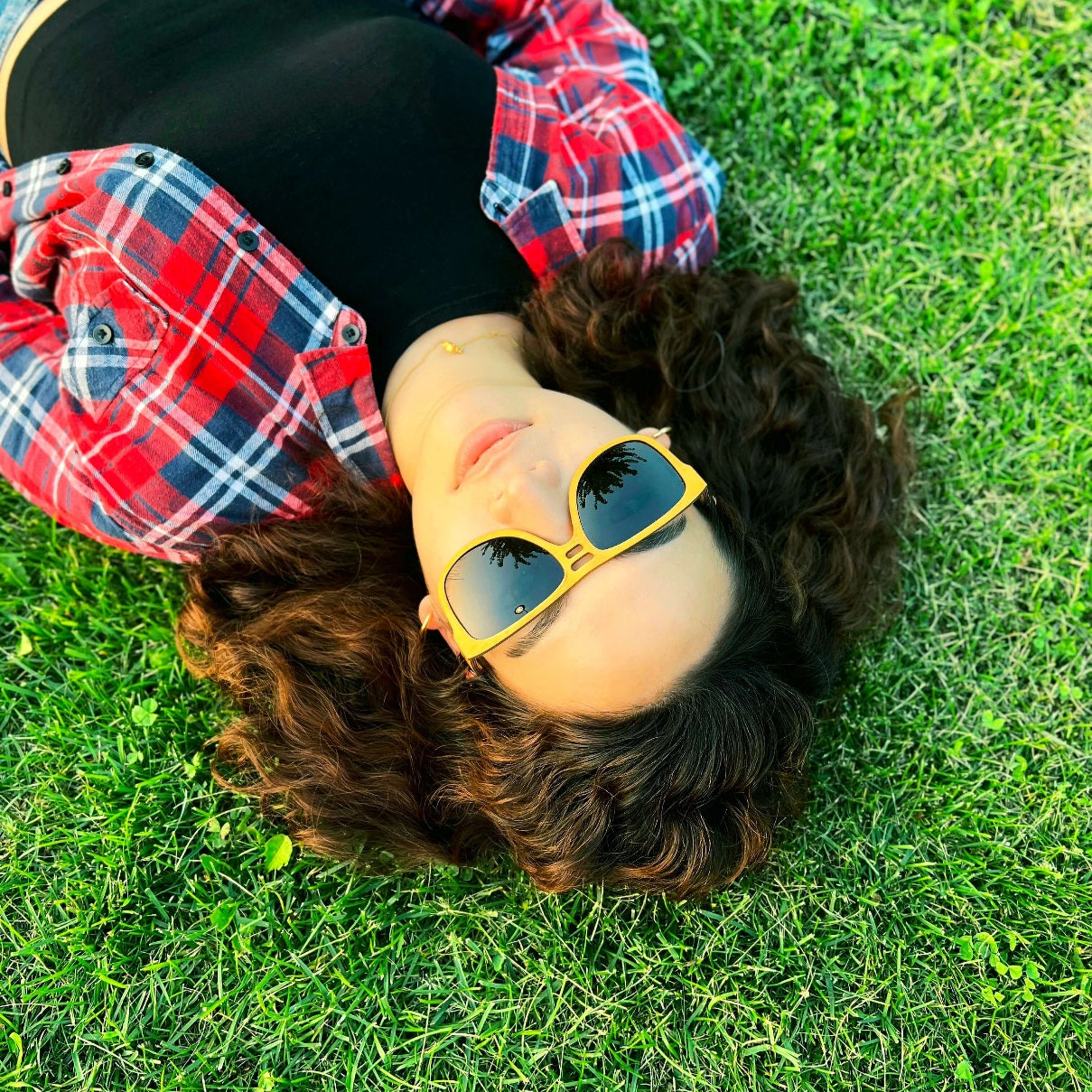 A woman wearing Yellowheart wood sunglasses, lying on the grass, enjoying the sun's warmth and relaxation.
