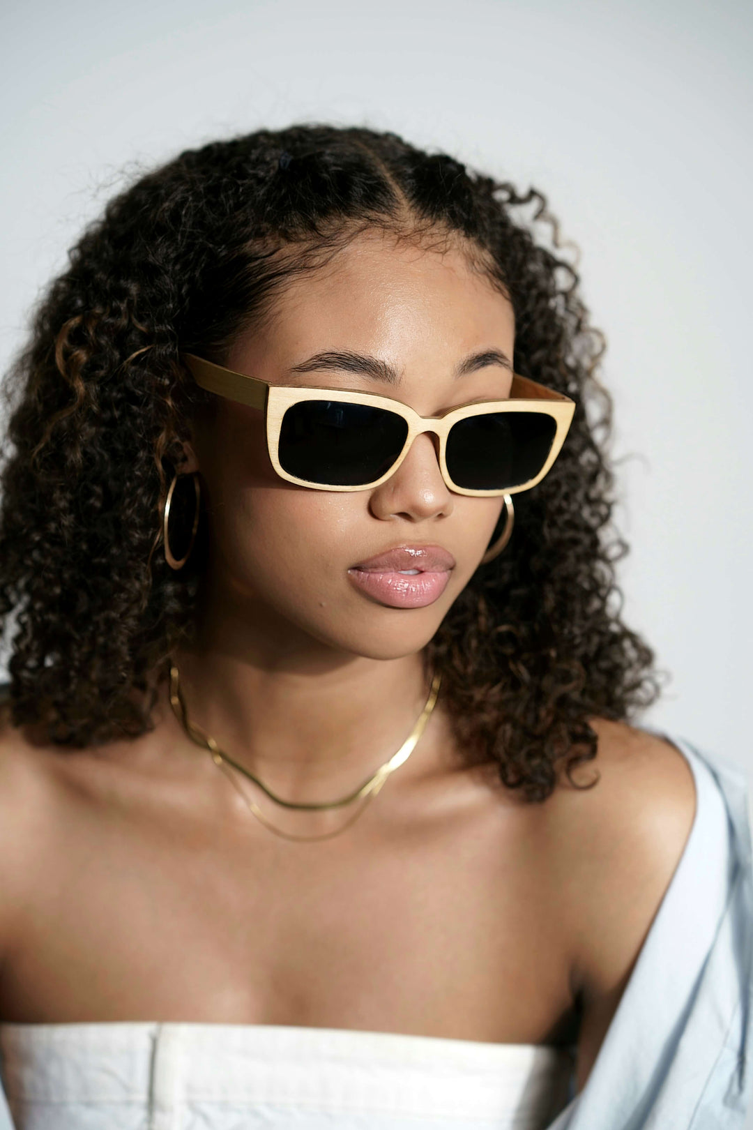 A woman with curly hair wearing handmade maple wood sunglasses with polarized lenses.