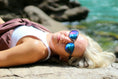 Load image into Gallery viewer, A woman laying on a rock, wearing wooden sunglasses, enjoying the serene surroundings.
