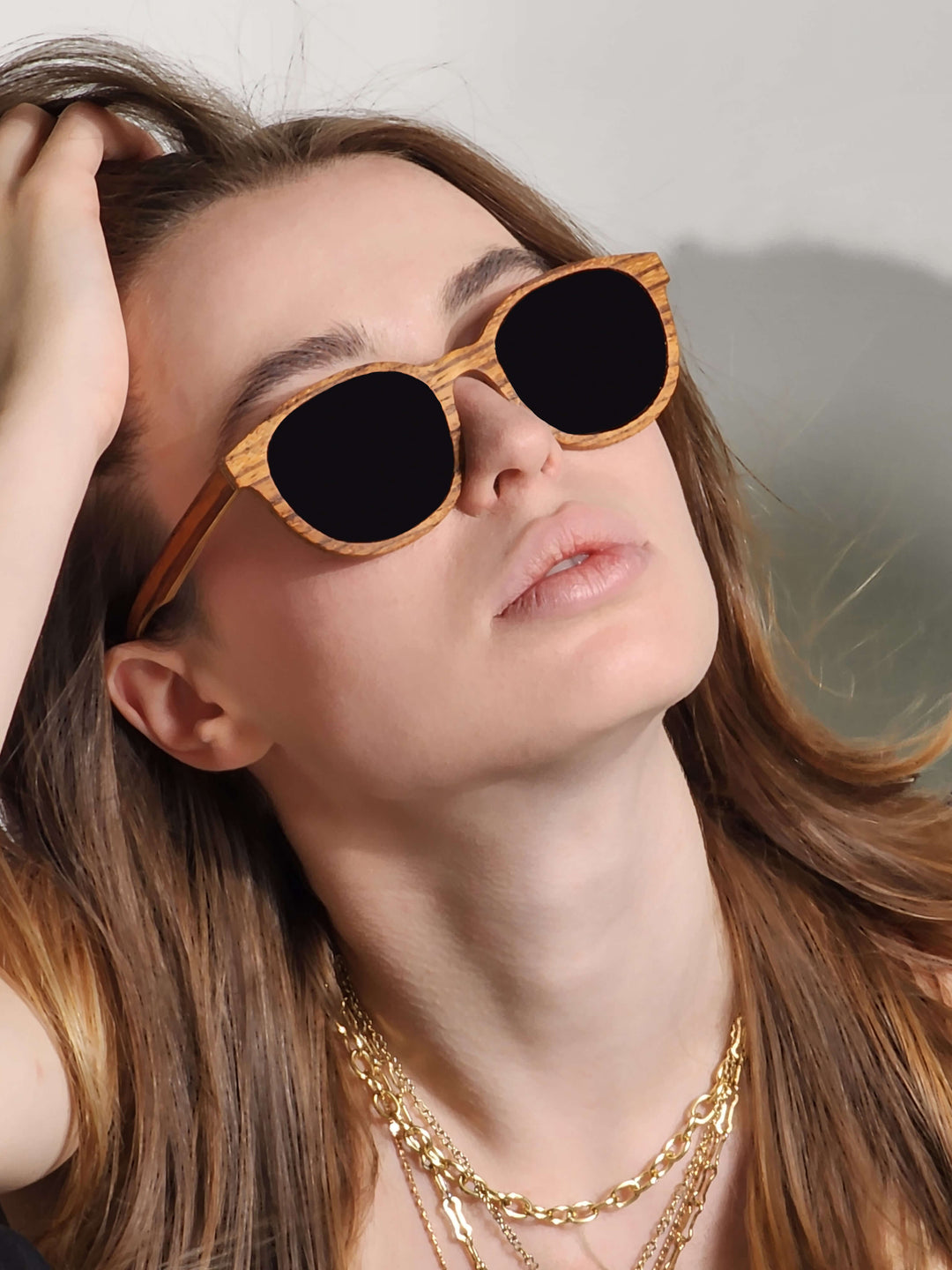  A stylish woman wearing Zebrawood wooden sunglasses with a gold chain around her neck.