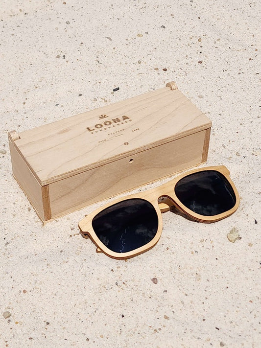 Maple wooden sunglasses with black polarized lenses and a box on sandy beach.