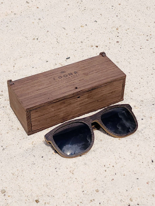 Wenge wooden sunglasses with black polarized lenses and a box on sandy beach.