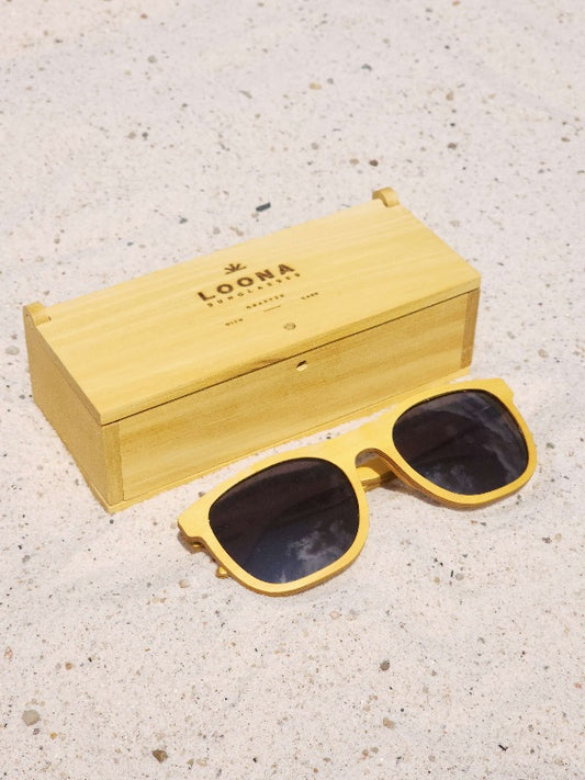Yellowheart wooden sunglasses with black polarized lenses and a box on sandy beach.