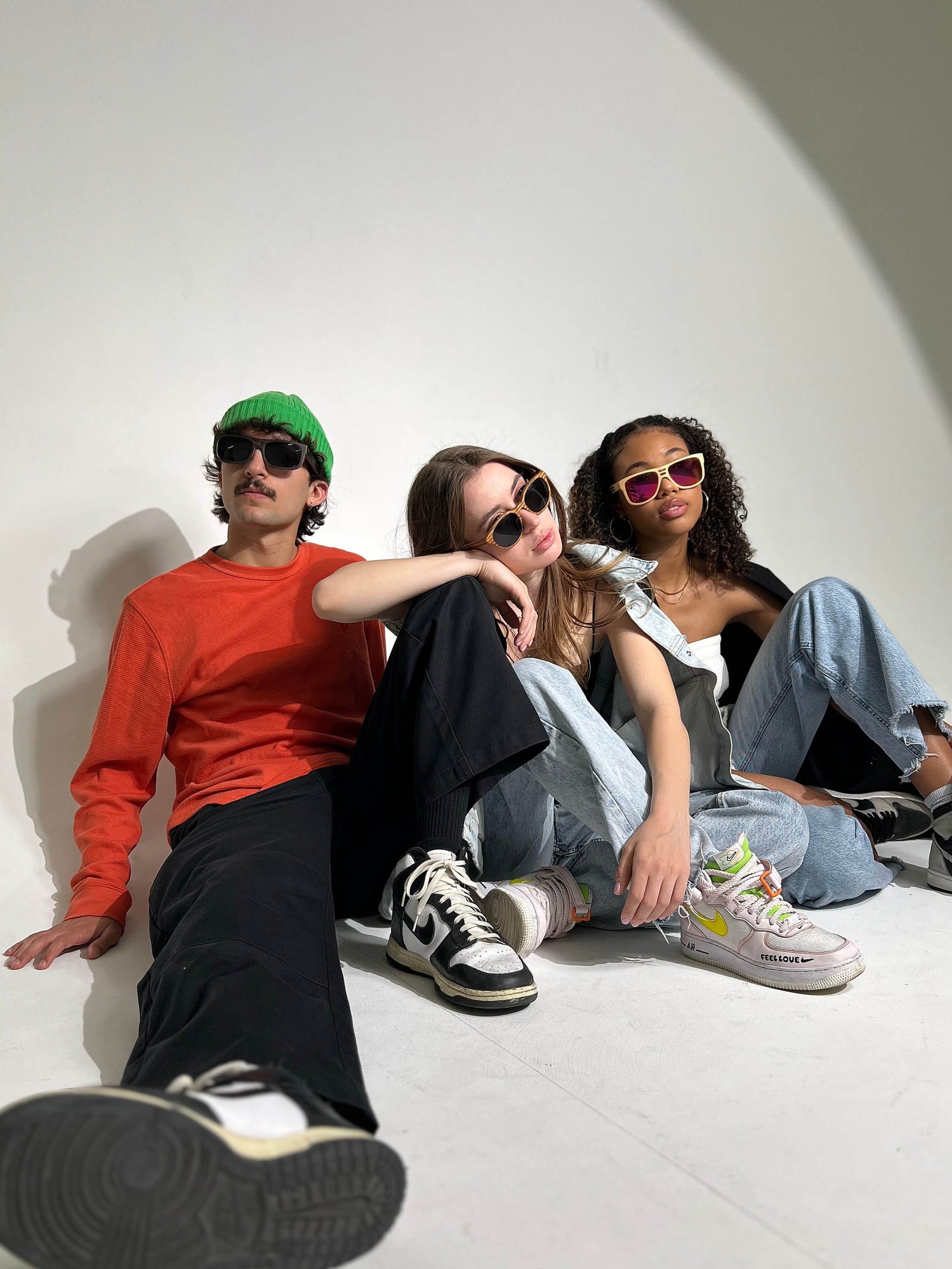 Three people sitting on the floor, wearing wooden sunglasses.