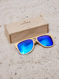 Load image into Gallery viewer, Maple wooden sunglasses with blue polarized lenses and a box on sandy beach.
