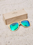 Load image into Gallery viewer, Maple wooden sunglasses with green polarized lenses and a box on sandy beach.
