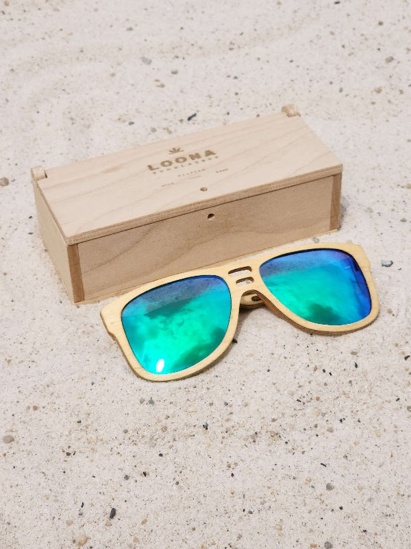 Maple wooden sunglasses with green polarized lenses and a box on sandy beach.