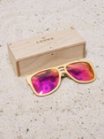 Load image into Gallery viewer, Maple wooden sunglasses with red polarized lenses and a box on sandy beach.
