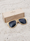 Load image into Gallery viewer, Maple wooden sunglasses with black polarized lenses and a box on sandy beach.
