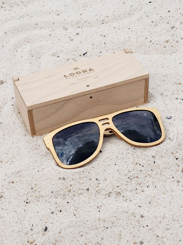 Maple wooden sunglasses with black polarized lenses and a box on sandy beach.