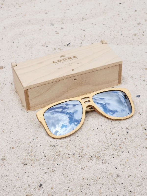 Maple wooden sunglasses with silver polarized lenses and a box on sandy beach.