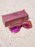 Load image into Gallery viewer, Purpleheart wooden sunglasses with red polarized lenses and a box on sandy beach.
