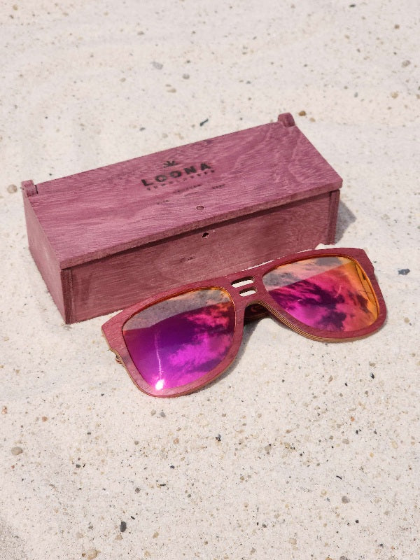 Purpleheart wooden sunglasses with red polarized lenses and a box on sandy beach.