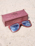 Load image into Gallery viewer, Purpleheart wooden sunglasses with silver polarized lenses and a box on sandy beach.
