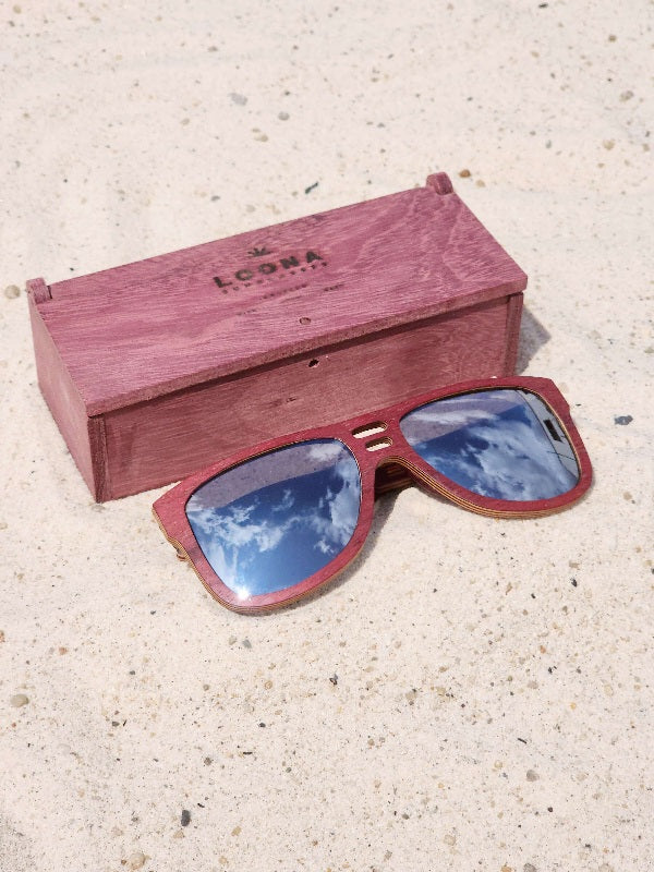 Purpleheart wooden sunglasses with silver polarized lenses and a box on sandy beach.