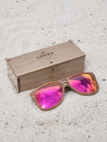Load image into Gallery viewer, Walnut wooden sunglasses with red polarized lenses and a box on sandy beach.
