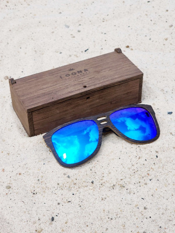 Wenge wooden sunglasses with blue polarized lenses and a box on sandy beach.