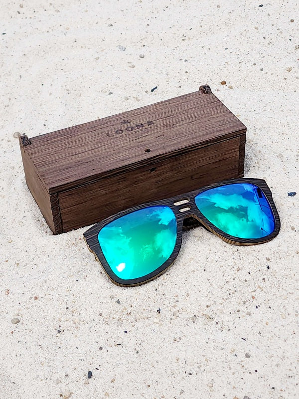 Wenge wooden sunglasses with green polarized lenses and a box on sandy beach.