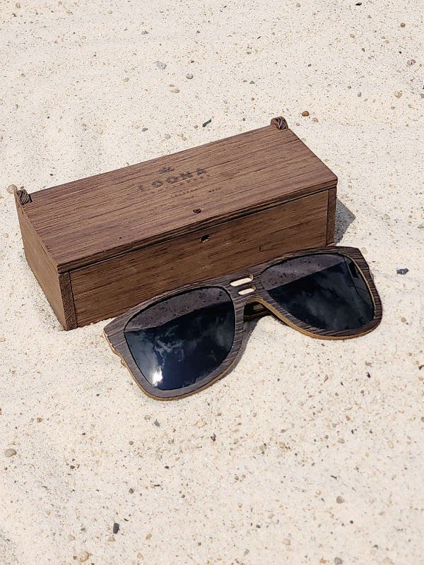 Wenge wooden sunglasses with black polarized lenses and a box on sandy beach.