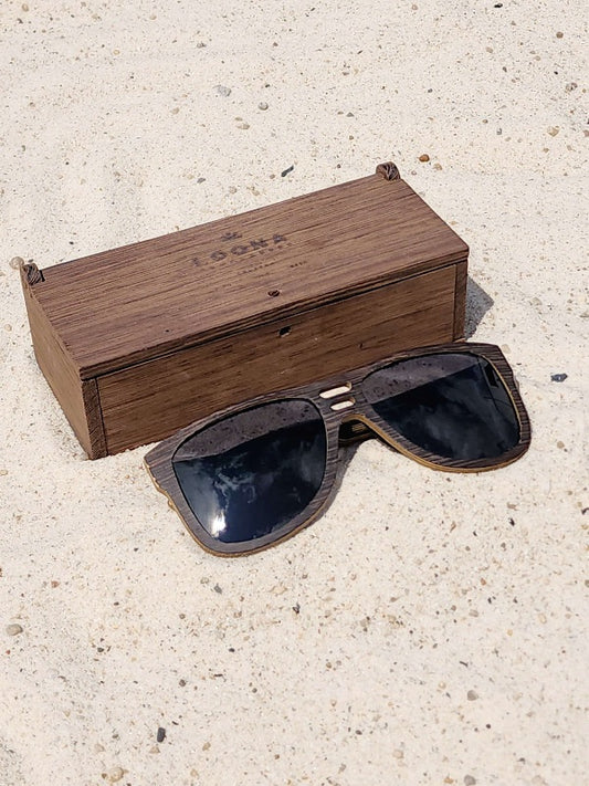 Wenge wooden sunglasses with black polarized lenses and a box on sandy beach.