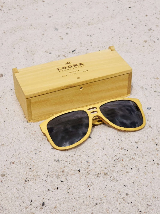 Yellowheart wooden sunglasses with black polarized lenses and a box on sandy beach.