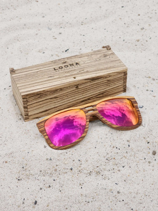 Zebrawood wooden sunglasses with red polarized lenses and a box on sandy beach.