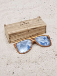 Load image into Gallery viewer, Zebrawood wooden sunglasses with silver polarized lenses and a box on sandy beach.
